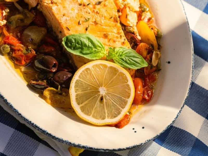 Delicious grilled salmon topped with lemon and basil on a sunlit table.